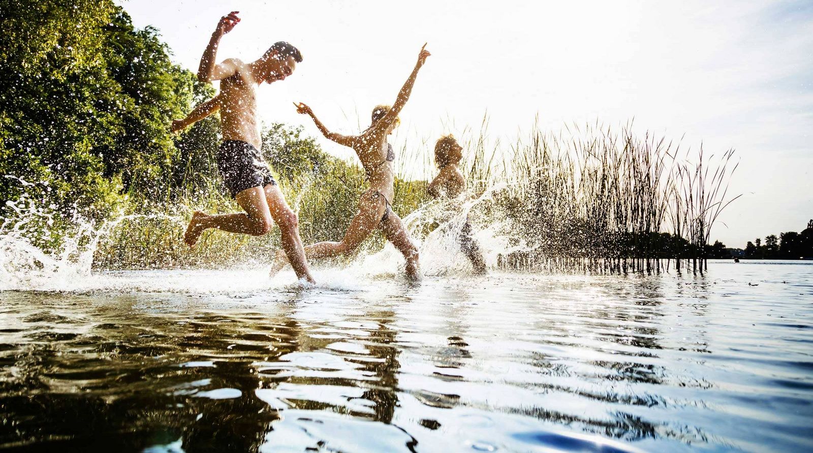 drei Leute rennen in das Wasser eines Sees 