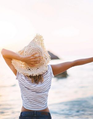Eine Frau mit einem Hut alleine am Meer