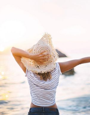 Eine Frau mit einem Hut alleine am Meer