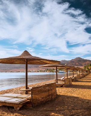Blick auf einen Strand in Aegypten am Meer mit Liegestühlen und Sonnenschirmen aus Stroh