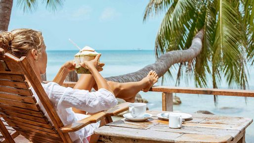 Frau mit einer Kokosnuss auf einem Liegestuhl am Meer