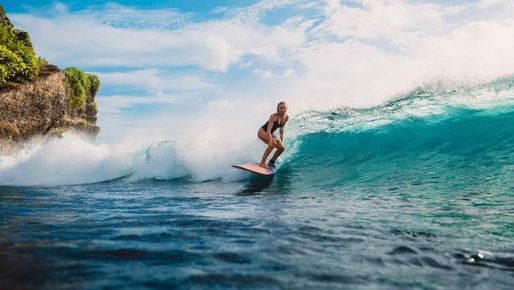 Frau surft auf einer Welle vor Bali